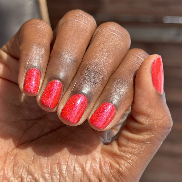 Hand with short nails painted vibrant pinky-red shimmer using Rodeo Queen - Gel polish in natural sunlight