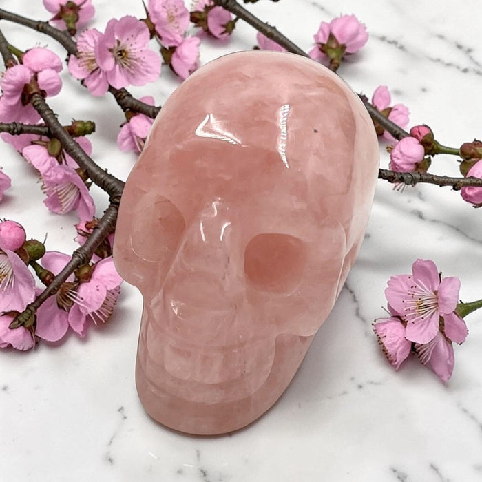 Pink crystal skull with cherry blossoms on a marble surface