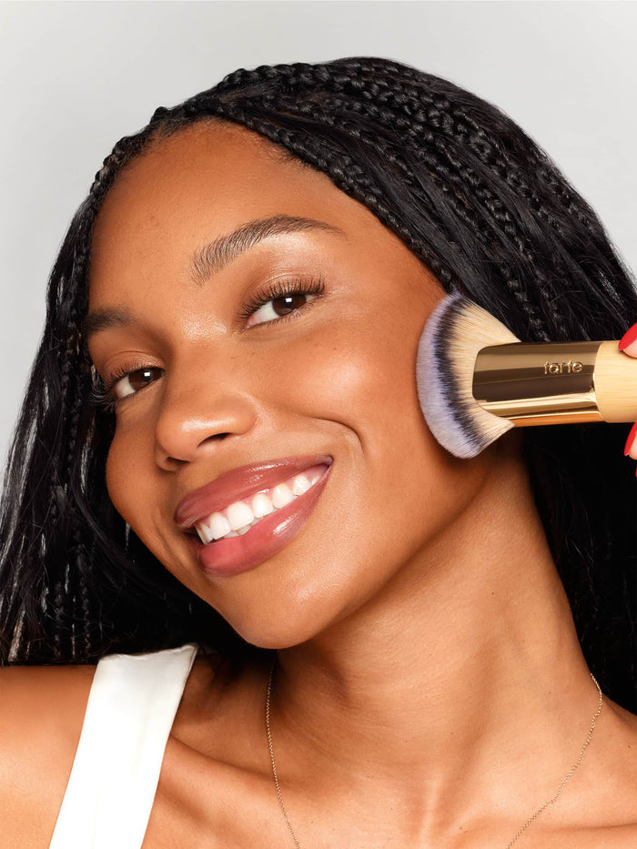 Woman applying makeup with a brush on a plain background