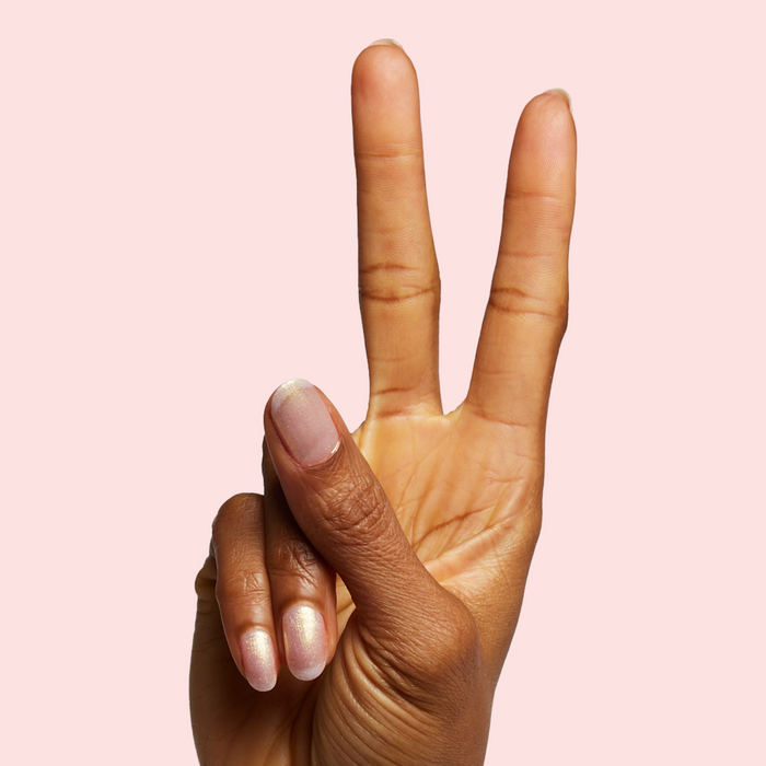 Hand with sheer pink iridescent Sugarcoat quick dry polish on natural skin against soft blush background
