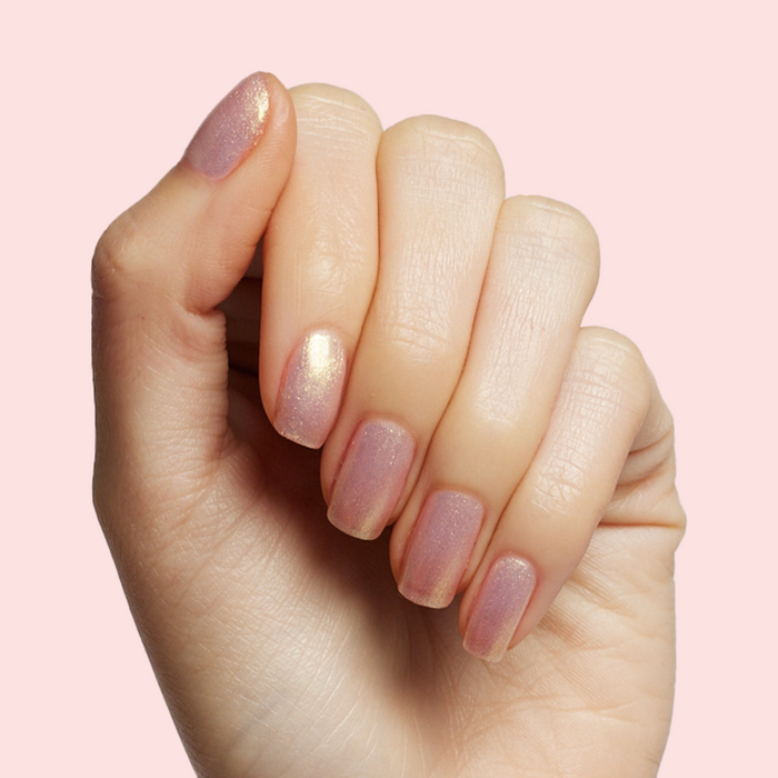 Hand showing sheer shimmery pink iridescent Sugarcoat quick dry polish manicure on natural skin against pale pink background