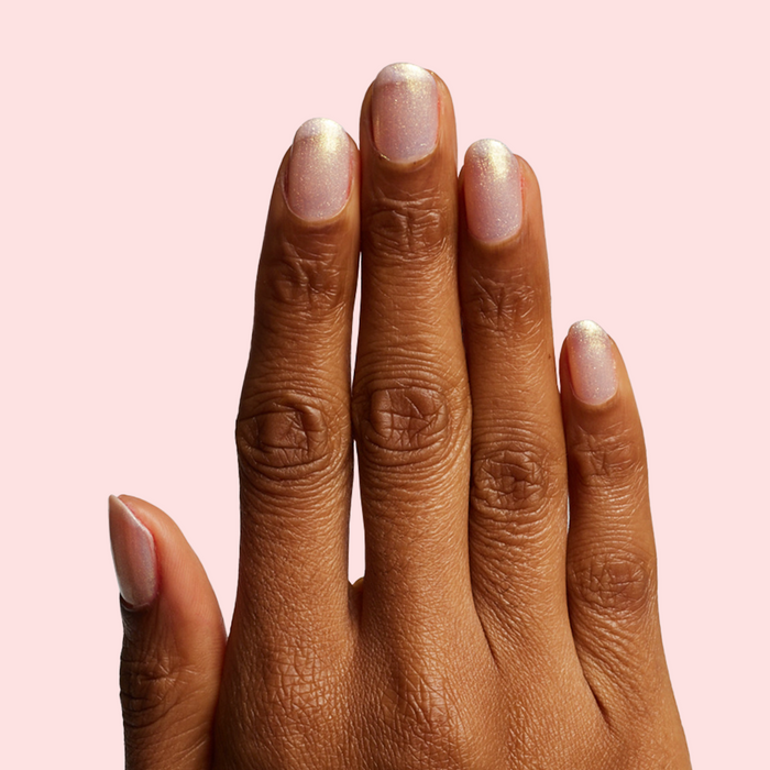 Hand with sheer shimmery pink iridescent Sugarcoat quick dry polish manicure on natural skin against pale pink background