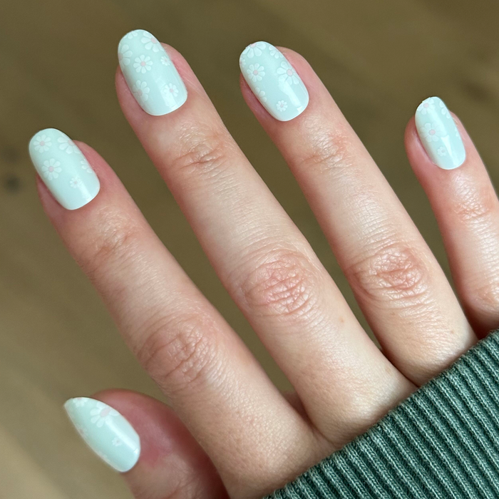 Teal Chrome Flower Shower - Press-On | Short | Round pastel teal press-on nails with subtle white daisy details on hand indoors